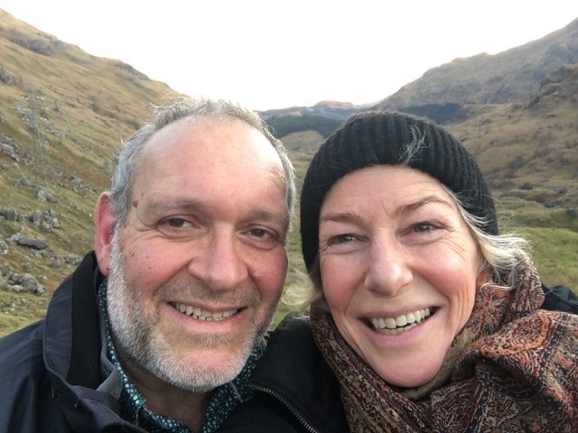 A selfie of a smiling man and woman in front of a mountain in Scotland