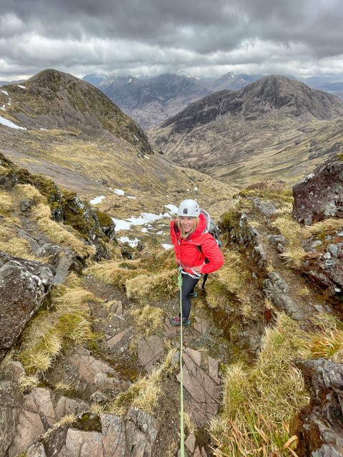 A woman in a red jacket climbing in Scotland 