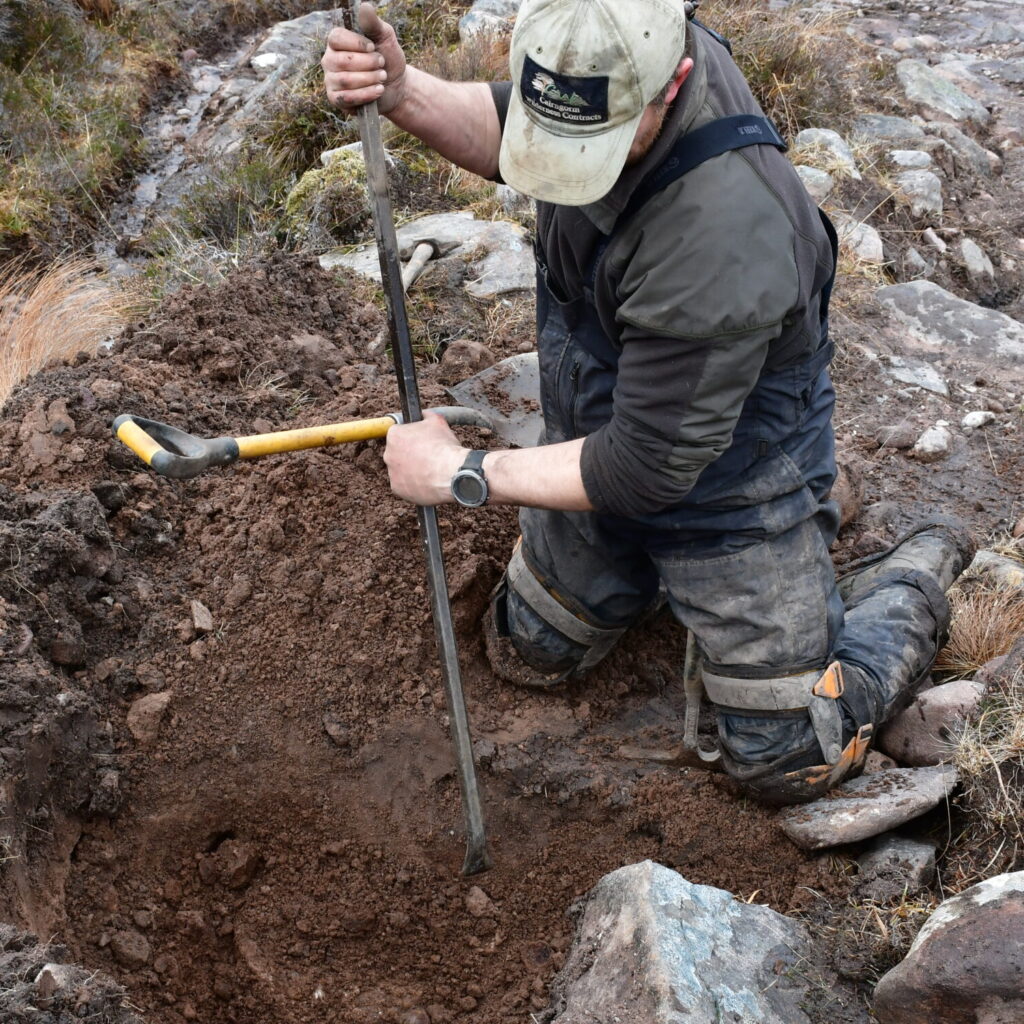 Contractor digs hole on mountain path on An Teallach